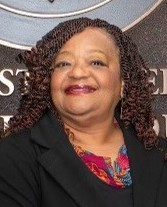 Portrait of Terrie Richardson, a council member, smiling in front of an emblematic backdrop, wearing a black blazer and colorful blouse.